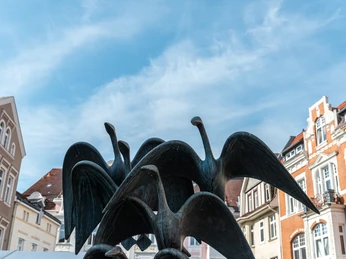 Skulpturengruppe aus Vögeln vor historischen Gebäuden unter klarem Himmel in Herford, Deutschland.