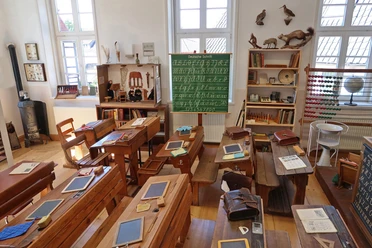 Historisches Klassenzimmer im Schulmuseum Delbrück mit Holzbänken, Tafeln und einem grünen Tafelbild.
