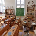 Historisches Klassenzimmer im Schulmuseum Delbrück mit Holzbänken, Tafeln und einem grünen Tafelbild.