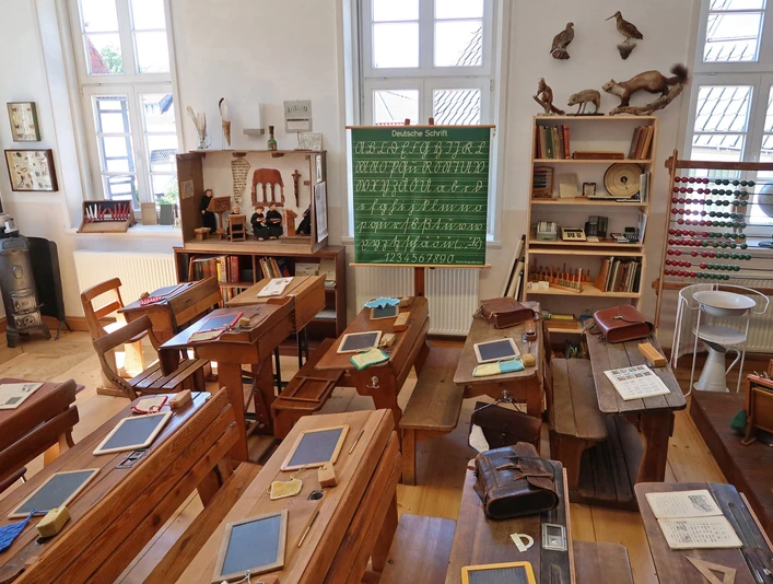 Historisches Klassenzimmer im Schulmuseum Delbrück Historisches Klassenzimmer im Schulmuseum Delbrück mit Holzbänken, Tafeln und einem grünen Tafelbild.
