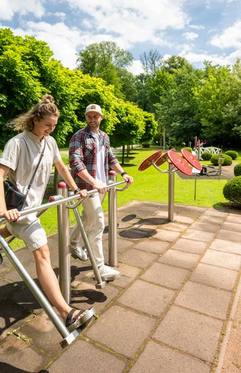Besucher genießen die Nutzung von Outdoor-Fitnessgeräten inmitten einer grünen Parklandschaft.