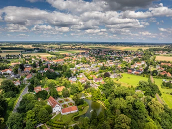 Luftaufnahme des Kurparks Bad Holzhausen mit grünen Wiesen, einem Teich und umliegenden Gebäuden.