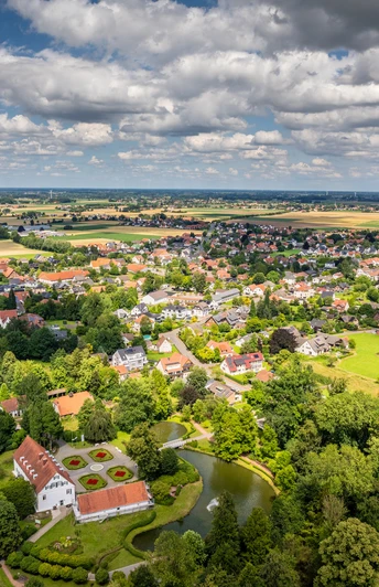 Luftaufnahme des Kurparks Bad Holzhausen mit grünen Wiesen, einem Teich und umliegenden Gebäuden.