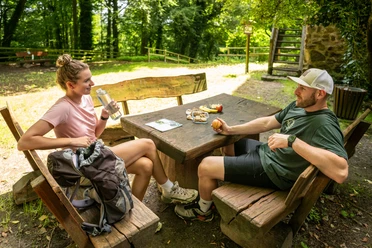 Burg Limberg Zwei Personen sitzen an einem Holztisch im Freien und unterhalten sich bei einer Rast im Grünen.
