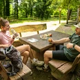 Burg Limberg Zwei Personen sitzen an einem Holztisch im Freien und unterhalten sich bei einer Rast im Grünen.