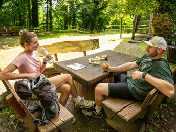 Burg Limberg Zwei Personen sitzen an einem Holztisch im Freien und unterhalten sich bei einer Rast im Grünen.