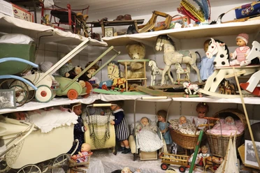 Spielzeugmuseum Historisches Spielzeugmuseum mit Puppen, Teddybären und Holzpferdchen auf Regalen bestückt.