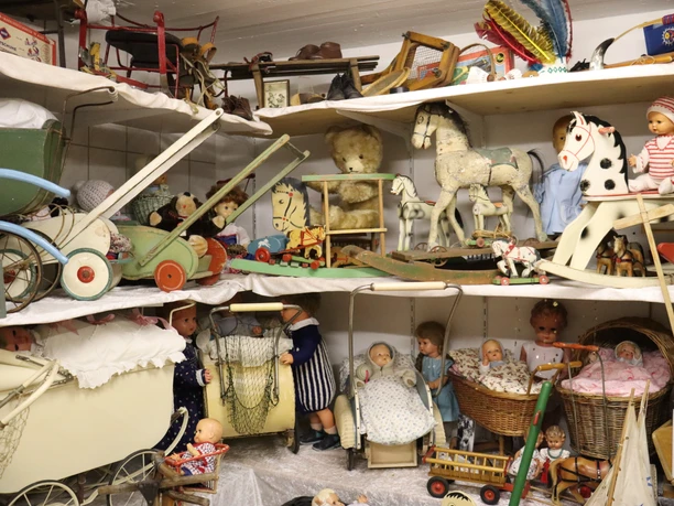 Spielzeugmuseum Historisches Spielzeugmuseum mit Puppen, Teddybären und Holzpferdchen auf Regalen bestückt.