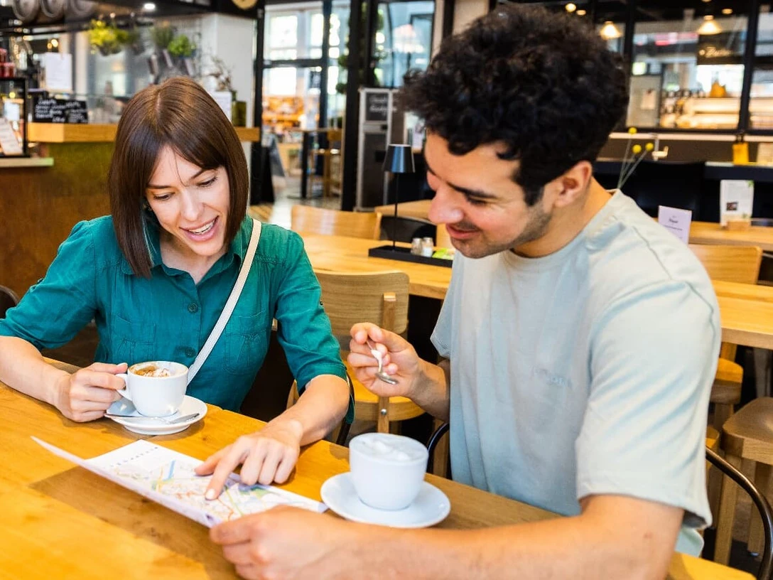 herford-Gastronomie-H Tornow 2-jpg.jpg Zwei Personen genießen Kaffee in einem modernen Café, während sie eine Karte betrachten.