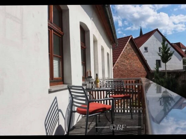 Fewo_Steinadler2-600x409.jpg Eine sonnige Terrasse mit Stühlen und Tisch, umgeben von weißen Gebäuden und roten Ziegeldächern.