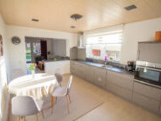 IMG_7945-200x133.jpg Moderne Küche mit grauen Einbaugeräten, einem Esstisch und viel Tageslicht durch große Fenster.