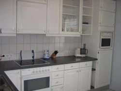 eggert1.jpeg Weiße Einbauküche mit Herd, Dunstabzug und Mikrowelle. Arbeitsfläche aus dunklem Material.