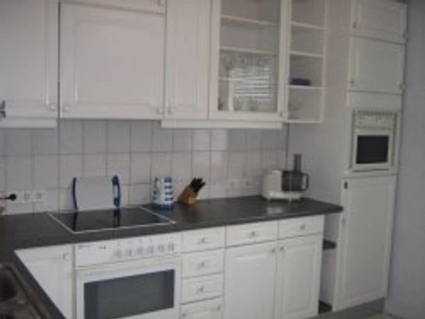 eggert1.jpeg Weiße Einbauküche mit Herd, Dunstabzug und Mikrowelle. Arbeitsfläche aus dunklem Material.