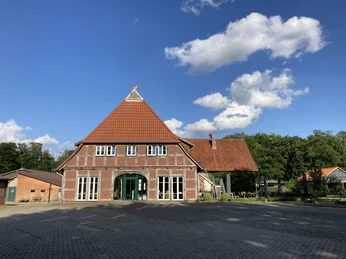 SpeicherKaffee Rotes Backsteinhaus mit rotem Ziegeldach und dunkelgrüner Eingangstür vor blauem Himmel.