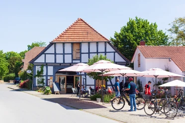 Radlerpause in Levern.jpg Eine Gruppe von Radfahrern pausiert vor einem Fachwerkhaus mit schattigen Sonnenschirmen in Levern.