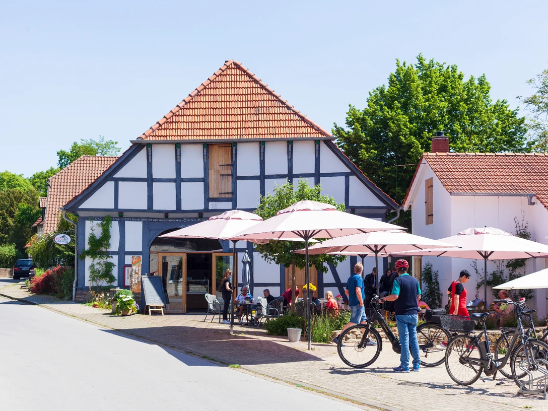 Radlerpause in Levern.jpg Eine Gruppe von Radfahrern pausiert vor einem Fachwerkhaus mit schattigen Sonnenschirmen in Levern.