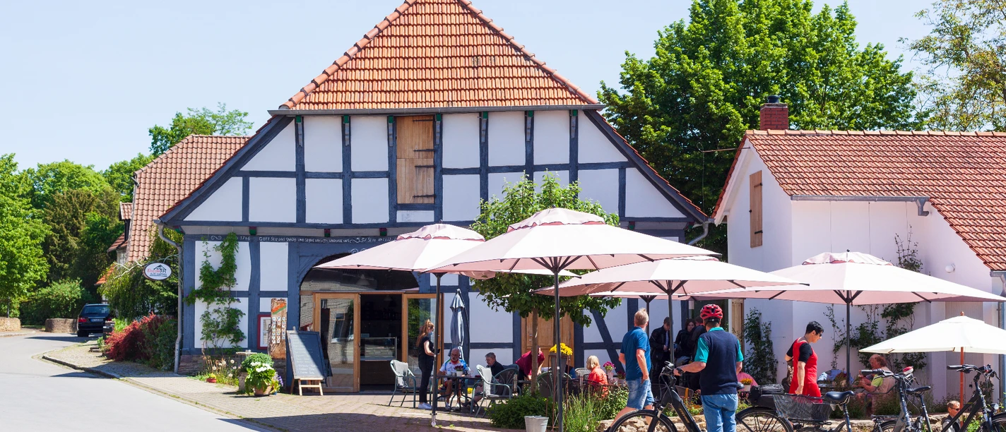 Radlerpause in Levern.jpg Eine Gruppe von Radfahrern pausiert vor einem Fachwerkhaus mit schattigen Sonnenschirmen in Levern.