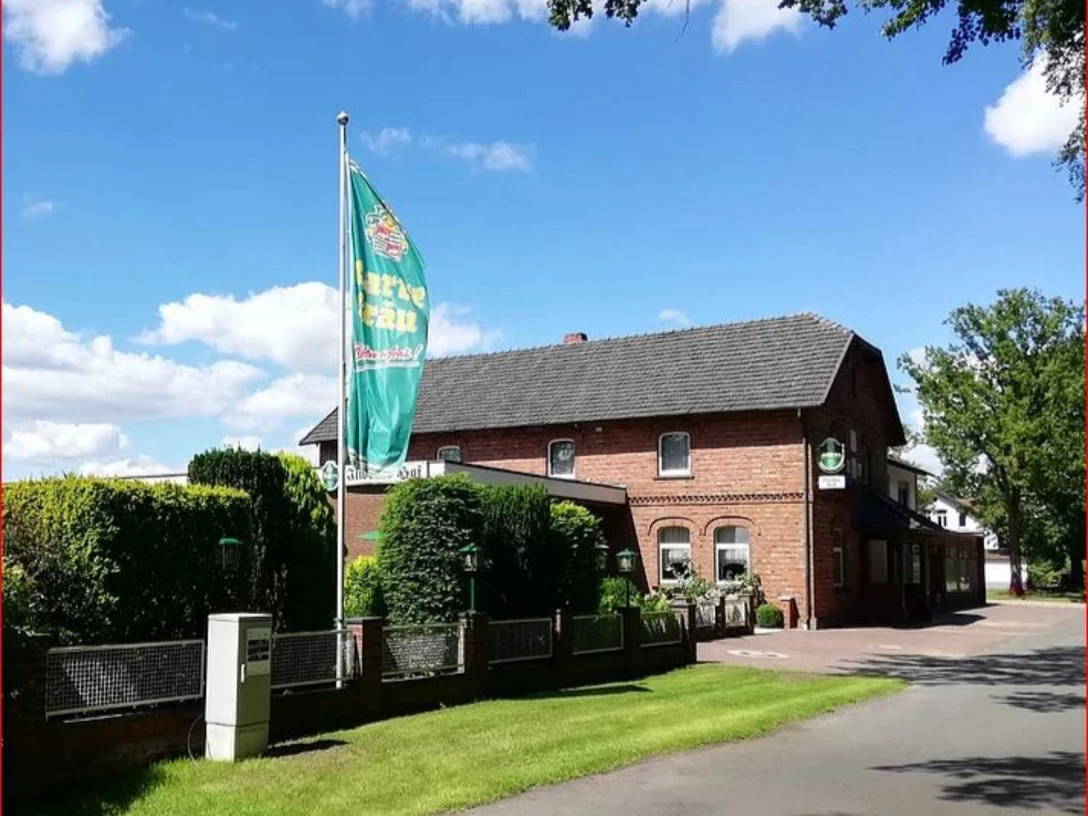 Ilweder_Hof.jpg Ein Backsteinhaus in ländlicher Umgebung mit einer großen Fahne und gepflegtem Garten.