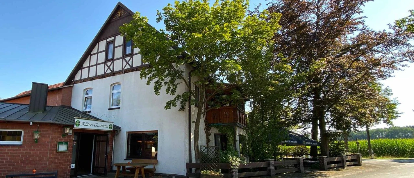 Fachwerkgebäude von Rüters Gasthaus mit überhängenden Bäumen, umgeben von sonnigem blauen Himmel.