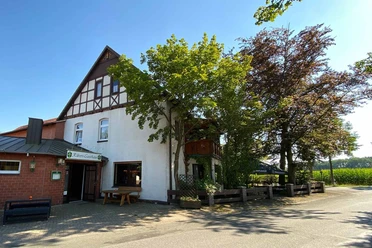Rüters Gasthaus Fachwerkgebäude von Rüters Gasthaus mit überhängenden Bäumen, umgeben von sonnigem blauen Himmel.