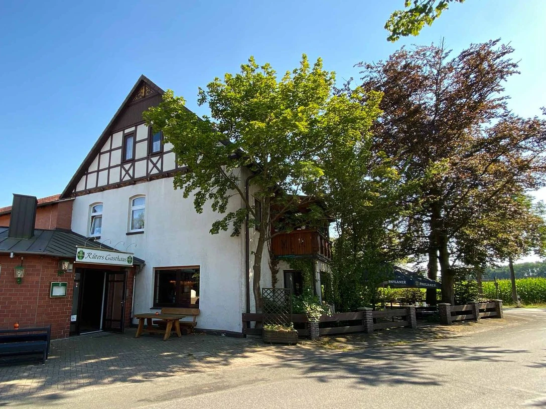 Rüters Gasthaus Fachwerkgebäude von Rüters Gasthaus mit überhängenden Bäumen, umgeben von sonnigem blauen Himmel.