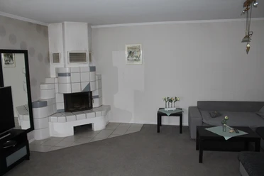 Stellmanns Gästehof Wohnraum mit modernem Kaminofen, grauem Ecksofa, Couchtisch und dezent dekorierten Wänden.