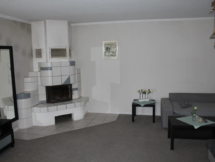 Stellmanns Gästehof Wohnraum mit modernem Kaminofen, grauem Ecksofa, Couchtisch und dezent dekorierten Wänden.