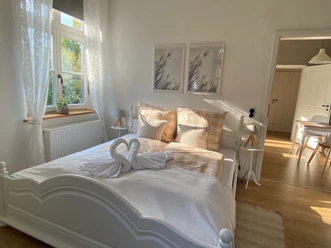 Lichte slaapkamer met tweepersoonsbed, twee zwanenhanddoekfiguren, houten vloer en moderne accenten.