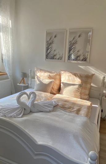 FeWo_Stiftsbrunnen_Schlafzimmer.jpg Helles Schlafzimmer mit Doppelbett, zwei Schwan-Handtuchfiguren, Holzfußboden und modernen Akzenten.