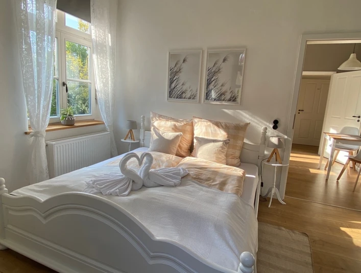 FeWo_Stiftsbrunnen_Schlafzimmer.jpg Helles Schlafzimmer mit Doppelbett, zwei Schwan-Handtuchfiguren, Holzfußboden und modernen Akzenten.