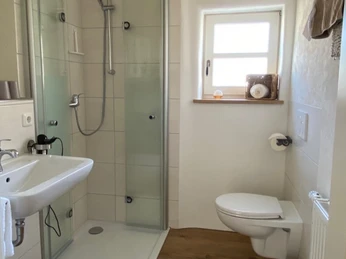 FeWo_Stiftsbrunnen_Bad.jpg Barrierefreies Badezimmer mit ebenerdiger Dusche, Wandschwenkarm und Toilette in neutralem Design.