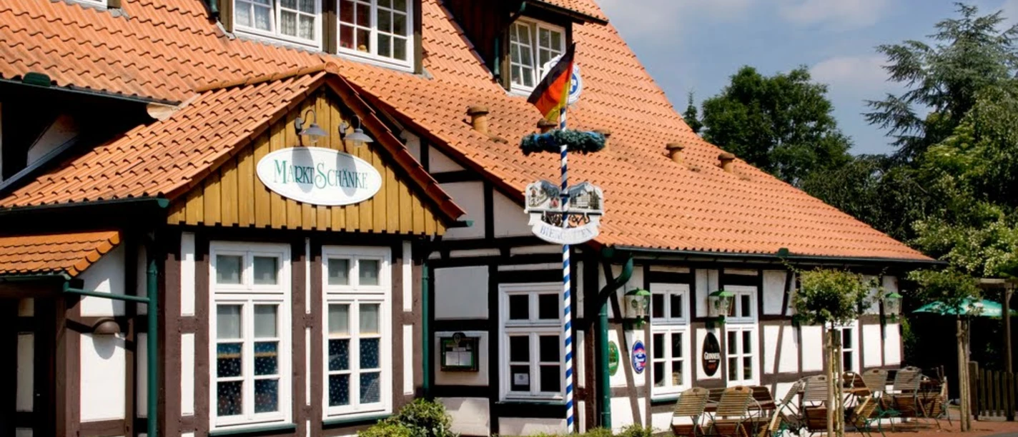 Ein Fachwerk-Gebäude mit Terrassensitzplätzen, deutschem Schild "Marktschänke" und rot gedecktem Dach.