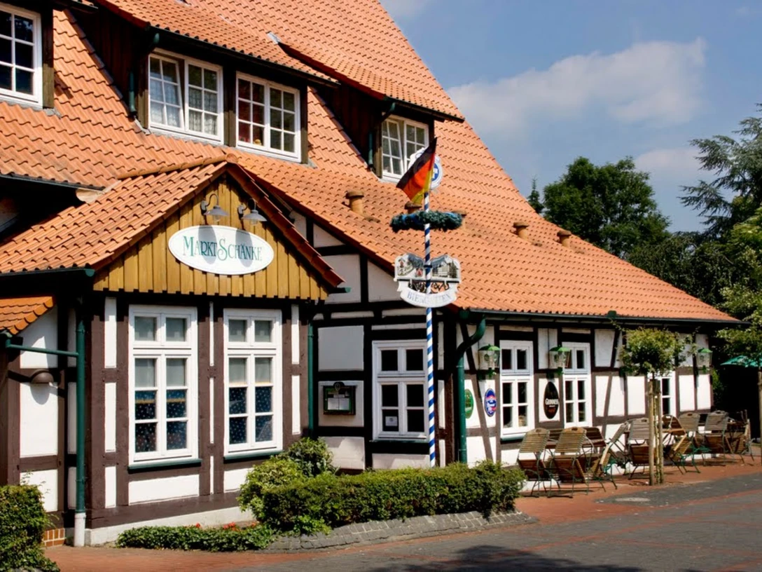 Marktschänke.jpg Ein Fachwerk-Gebäude mit Terrassensitzplätzen, deutschem Schild "Marktschänke" und rot gedecktem Dach.