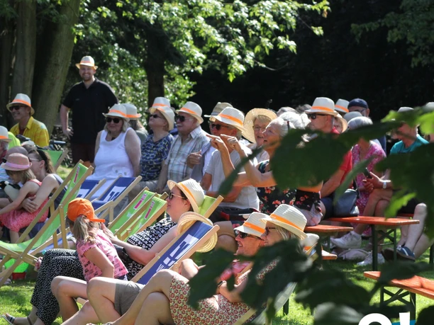 Herford-Mein Sommer Meine Stadt - Pro Herford GmbH 2.jpg Eine Gruppe von Menschen entspannt im Freien auf Liegestühlen und Bänken unter schattenspendenden Bäumen.