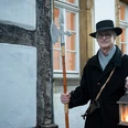 Nachtwächter Roland Zöller (3).jpg Ein Nachtwächter in historischer Kleidung steht mit Laterne und Hellebarde vor einem alten Fachwerkhaus.