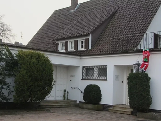 Gezellig wit huis met dakspanen en een kerstman die in een heg klimt.