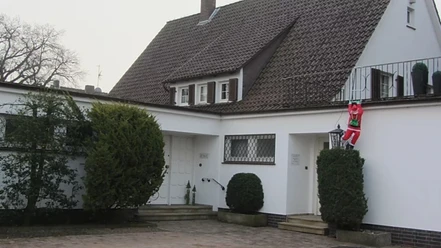 Apartment_Stemwede.jpg Gemütliches weißes Haus mit Dachschindeln und einem Weihnachtsmann, der an einer Hecke klettert.