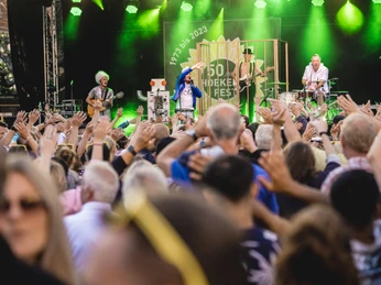 DSCF2990.jpg Menschenmenge genießt ein Open-Air-Konzert mit Band auf Bühne, während Hände in die Luft gereckt werden.