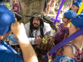 Hoekerfest2019_lowres_085.jpg Ein Pirat mit Schatzkiste umringt von Kindern in blauen Mützen und bunten Luftballons.