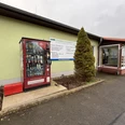 Proviantomat Standort Struppen Landfleischerei Roter Verkaufsautomat mit Lebensmitteln vor einem hellgrünen Gebäude, daneben ein Schild mit Angeboten und eine kleine, konische Tanne.Red vending machine with food in front of a light green building, next to it a sign with offers and a small, conical fir tree.Červený automat s jídlem před světle zelenou budovou, vedle něj cedule s nabídkami a malá kuželovitá jedle.Czerwony automat z jedzeniem przed jasnozielonym budynkiem, obok znak z ofertami i mała, stożkowa jodła.Rode automaat met eten voor een lichtgroen gebouw, ernaast een bord met aanbiedingen en een kleine, kegelvormige dennenboom.Distributore automatico rosso di cibo davanti a un edificio verde chiaro, accanto a un cartello con offerte e un piccolo abete conico.