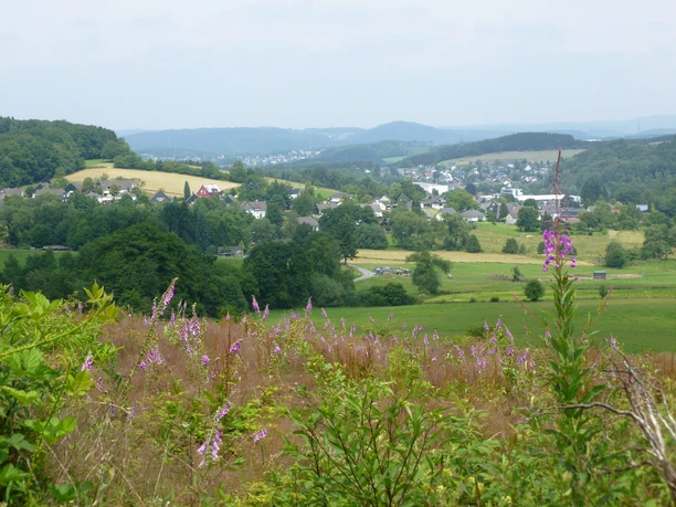 Bierweg <p>Landschaftspanorama bei Wiehl: Grüne Hügel, Wiesen und ein Dorf im Tal bei leicht bewölktem Himmel.</p>