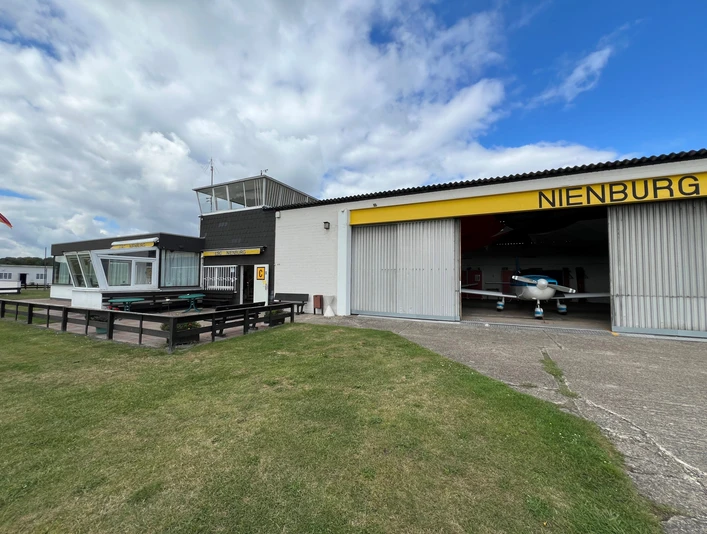 Flugplatz mit Hangars und einer gelben Markierung "Nienburg", Wiese im Vordergrund.