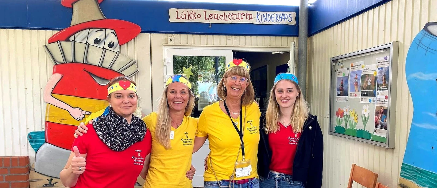 Kinderhaus-Team Four employees of the Lükko lighthouse children's home stand laughing in front of the entrance with children.