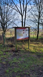 Informationstafel im Wald, umgeben von kahlen Bäumen, zeigt Wanderweg über bewaldetes Gebiet.