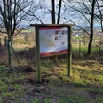 Informationstafel im Wald, umgeben von kahlen Bäumen, zeigt Wanderweg über bewaldetes Gebiet.