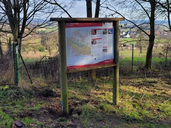 Waldweg Hille Informationstafel im Wald, umgeben von kahlen Bäumen, zeigt Wanderweg über bewaldetes Gebiet.