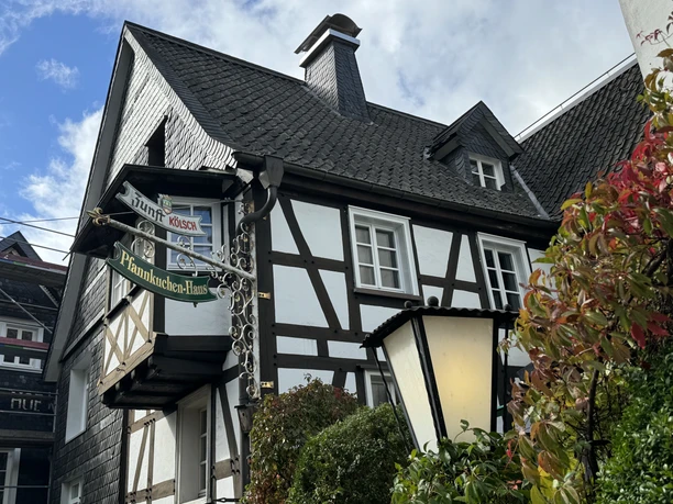 Pfannkuchenhaus Nümbrecht - Außenansicht Fachwerkhaus mit Schild "Pfannkuchen-Haus" unter blauem Himmel und herbstlichem Laub im Vordergrund.