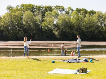 Naturbadesee Mindenerwald Familie spielt am See auf einer grünen Wiese; im Hintergrund ein ruhiger Natursee.