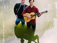 Zwei Männer stehen im Wasser, einer hält eine Gitarre, Spiegelung im Wasser sichtbar.