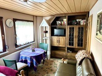 FeWo Mira 1 Herford-Stanojevic (6).jpg Wohnzimmer mit gemütlicher Sitzecke, Holzmöbeln, TV und dekorativem Tisch in einer Ferienwohnung.